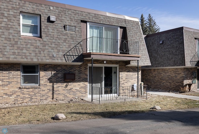 back of house featuring mansard roof, brick siding, a balcony, and a shingled roof