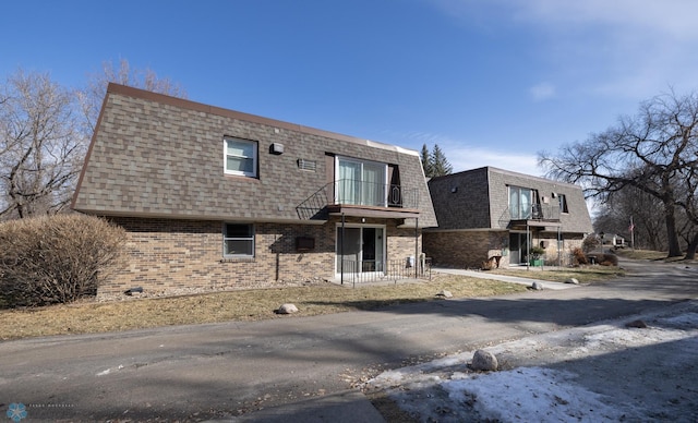 exterior space with mansard roof, brick siding, roof with shingles, and a balcony