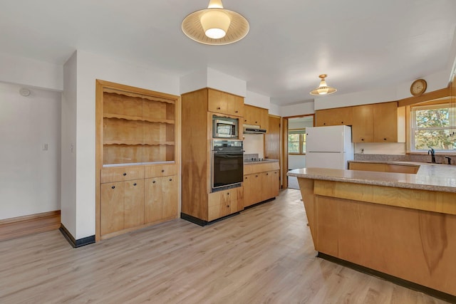 kitchen featuring light wood-style floors, a peninsula, light countertops, black appliances, and a sink