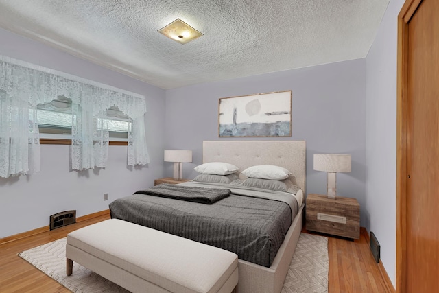 bedroom with a textured ceiling, light wood finished floors, and baseboards