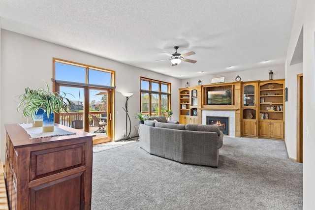 carpeted living area with a glass covered fireplace, a ceiling fan, and a textured ceiling
