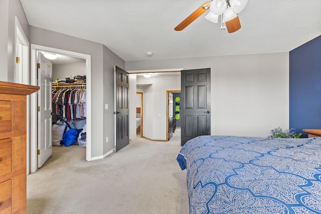 bedroom with light colored carpet, a walk in closet, baseboards, a closet, and ceiling fan