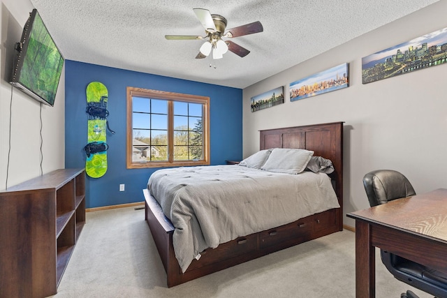 bedroom featuring light colored carpet, an office area, a textured ceiling, a ceiling fan, and baseboards