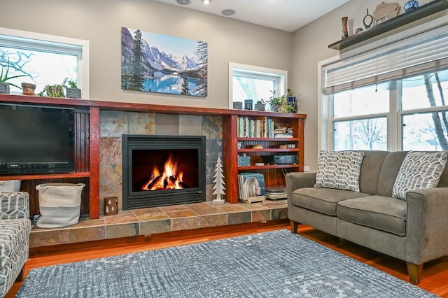 living room featuring a wealth of natural light, a tiled fireplace, and wood finished floors