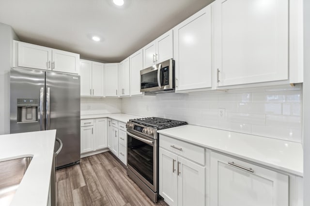 kitchen with light countertops, backsplash, appliances with stainless steel finishes, light wood-style floors, and white cabinetry