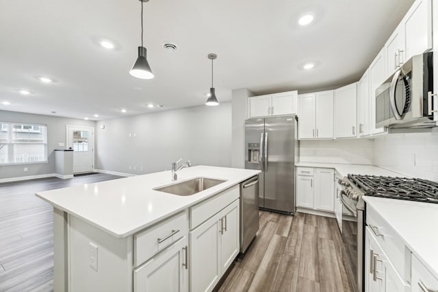 kitchen with appliances with stainless steel finishes, a sink, light countertops, light wood-style floors, and backsplash