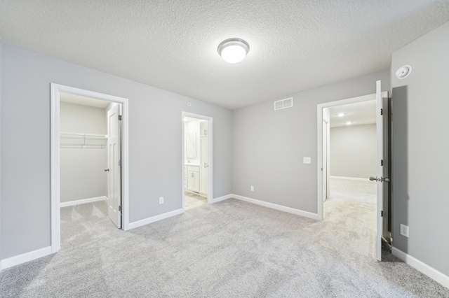 unfurnished bedroom featuring visible vents, light colored carpet, a spacious closet, and baseboards