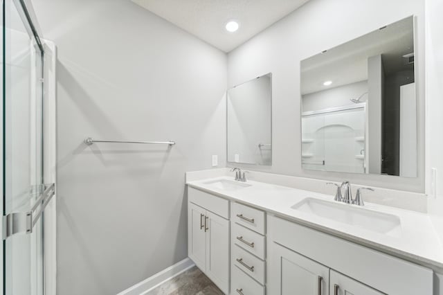 bathroom with double vanity, baseboards, an enclosed shower, and a sink