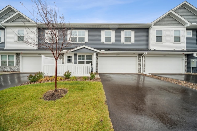 townhome / multi-family property featuring a front yard, stone siding, driveway, and an attached garage