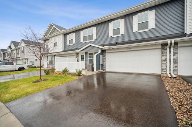 view of property featuring stone siding, a residential view, fence, and aphalt driveway