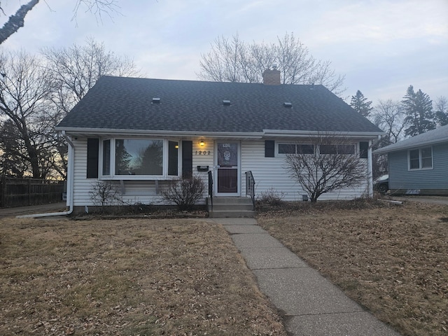 single story home featuring a shingled roof, a chimney, and a front lawn