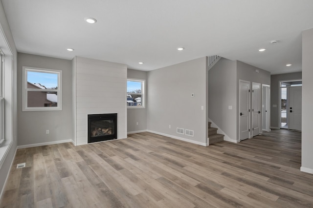 unfurnished living room featuring stairs, a fireplace, a wealth of natural light, and light wood-style floors