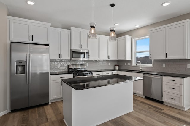 kitchen with dark countertops, appliances with stainless steel finishes, a sink, and wood finished floors