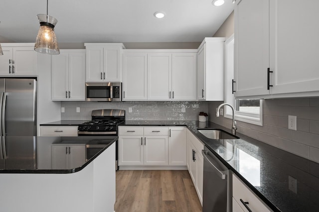 kitchen featuring light wood-style flooring, a sink, white cabinetry, hanging light fixtures, and appliances with stainless steel finishes