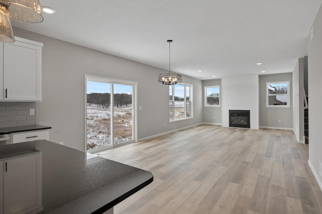 unfurnished dining area with recessed lighting, a fireplace, baseboards, light wood-style floors, and stairway