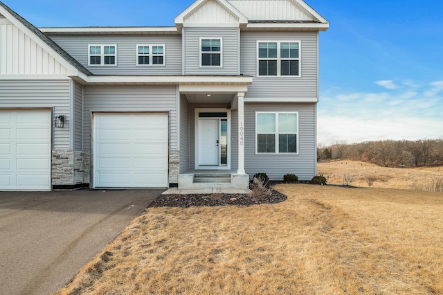 view of front of house with aphalt driveway, board and batten siding, an attached garage, and a front lawn