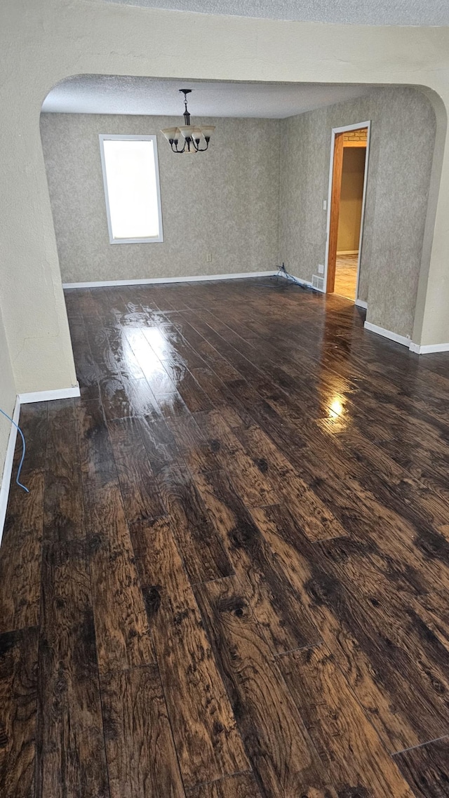 unfurnished room with baseboards, visible vents, arched walkways, dark wood-style floors, and a textured ceiling