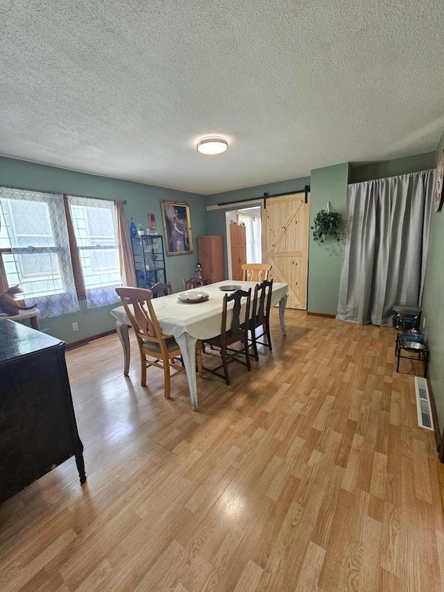 dining area featuring visible vents, light wood-style flooring, a barn door, a textured ceiling, and baseboards