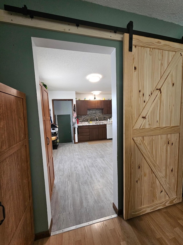 hall with light wood finished floors, a barn door, a textured ceiling, and a sink