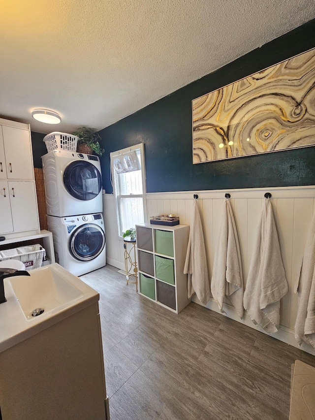 washroom with stacked washer and clothes dryer, wainscoting, a sink, a textured ceiling, and laundry area