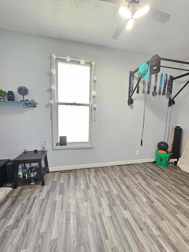 interior space with visible vents, wood finished floors, a ceiling fan, and baseboards