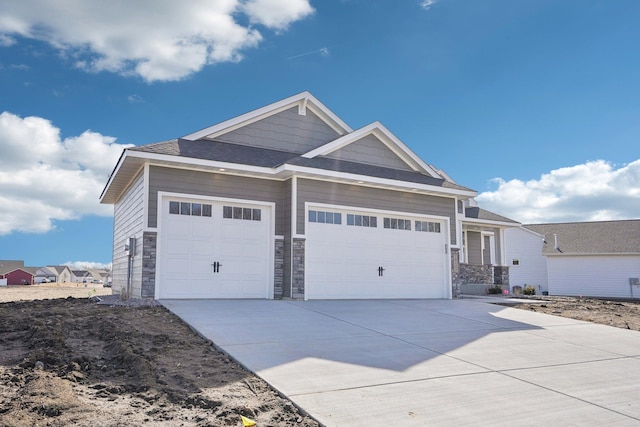 view of front facade featuring stone siding, concrete driveway, a garage, and a shingled roof