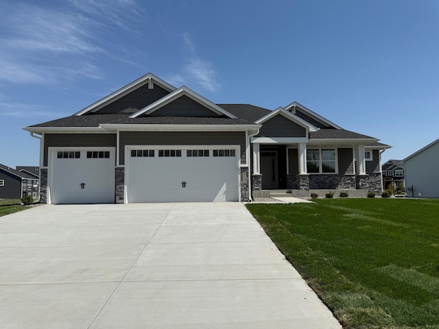craftsman-style house with a front yard, driveway, a garage, stone siding, and covered porch