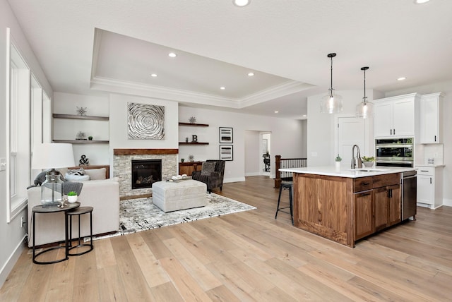 kitchen featuring light wood finished floors, open floor plan, a kitchen island with sink, a tray ceiling, and light countertops