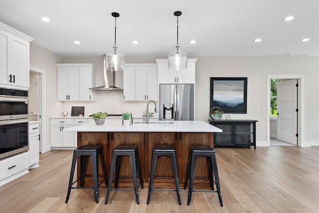 kitchen featuring stainless steel appliances, white cabinets, light countertops, wall chimney range hood, and decorative backsplash