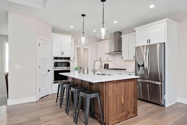 kitchen featuring appliances with stainless steel finishes, a breakfast bar, light wood-type flooring, wall chimney range hood, and a sink