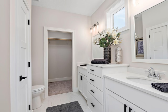 bathroom with marble finish floor, vanity, toilet, and a spacious closet