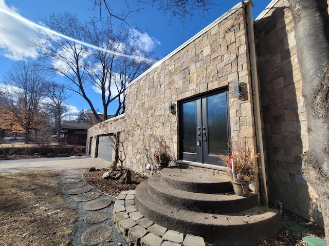 entrance to property with a garage, stone siding, driveway, and french doors