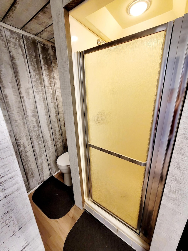 bathroom with a stall shower, toilet, and wood finished floors