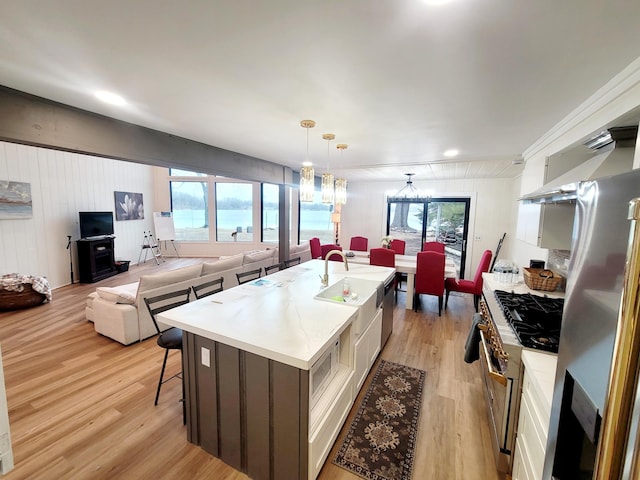 kitchen featuring a kitchen island with sink, appliances with stainless steel finishes, light countertops, a breakfast bar, and light wood-style flooring