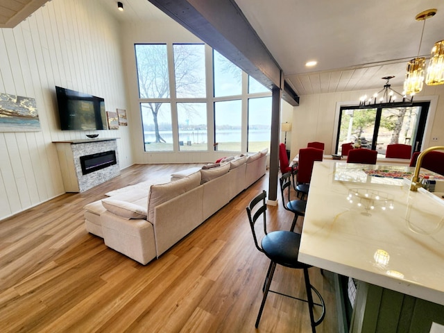 living area with wooden walls, lofted ceiling with beams, a notable chandelier, a glass covered fireplace, and wood finished floors
