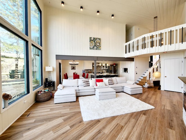 living area featuring a towering ceiling, wood walls, light wood-type flooring, stairway, and an inviting chandelier