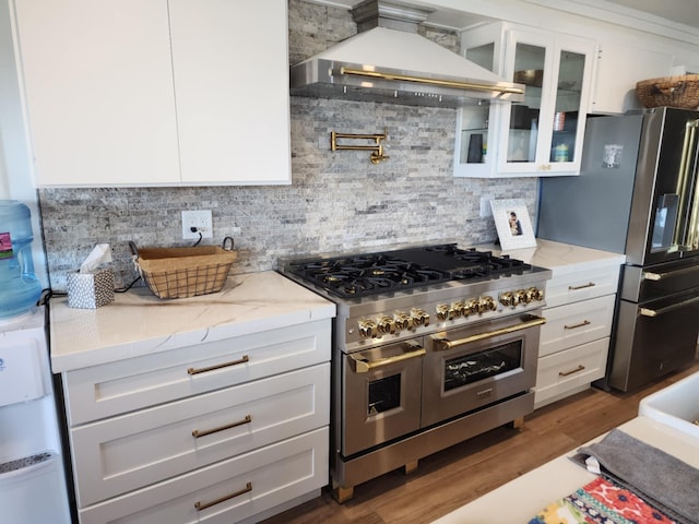 kitchen with wall chimney range hood, stainless steel appliances, white cabinets, and glass insert cabinets