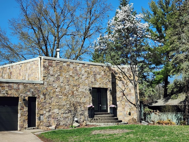 exterior space with stone siding, a garage, entry steps, a yard, and driveway