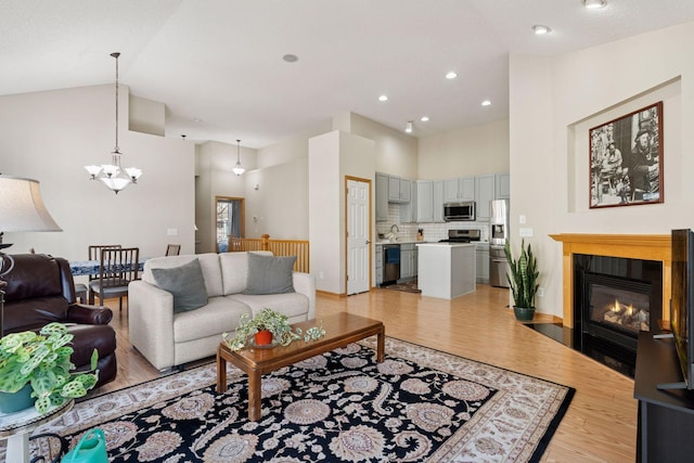 living area with baseboards, a glass covered fireplace, light wood-type flooring, high vaulted ceiling, and a notable chandelier