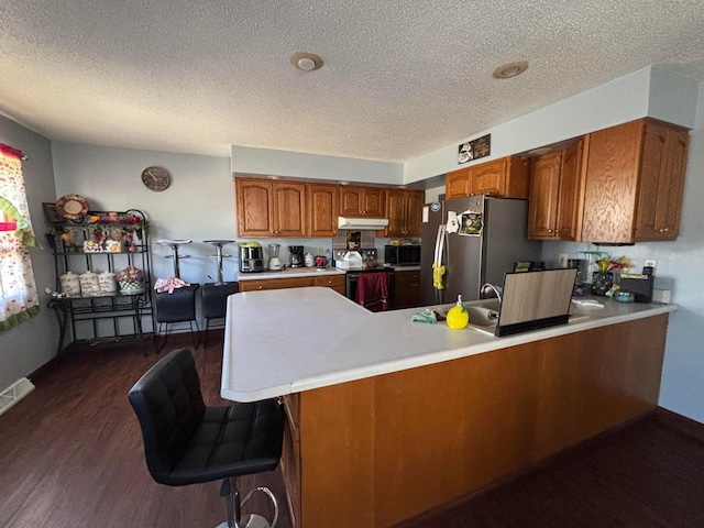 kitchen featuring a peninsula, range with electric stovetop, light countertops, freestanding refrigerator, and brown cabinetry