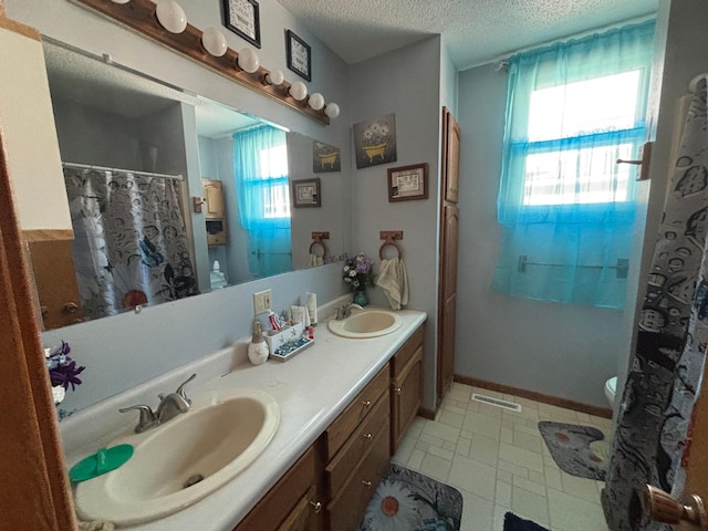 bathroom with double vanity, a textured ceiling, visible vents, and a sink