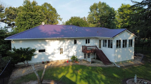 rear view of property featuring a deck, stairs, metal roof, and a lawn