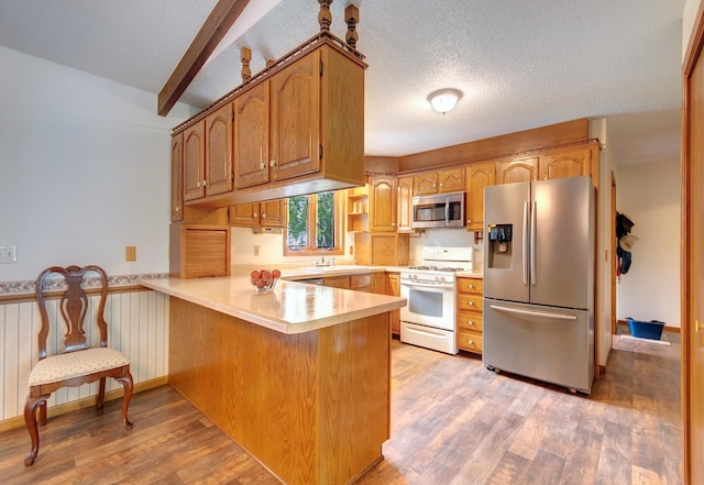 kitchen with stainless steel appliances, light wood-style floors, wainscoting, a textured ceiling, and a peninsula