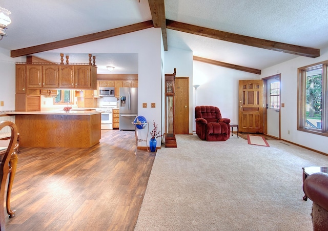 kitchen with a textured ceiling, a peninsula, open floor plan, appliances with stainless steel finishes, and brown cabinets