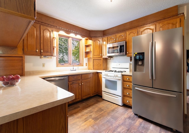 kitchen featuring brown cabinets, light countertops, appliances with stainless steel finishes, dark wood-type flooring, and a sink