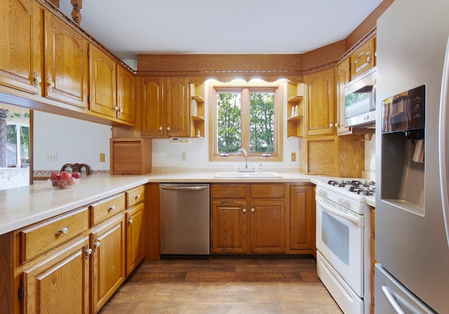 kitchen featuring appliances with stainless steel finishes, brown cabinets, wood finished floors, open shelves, and a sink