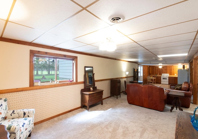 carpeted living area featuring a wainscoted wall, a drop ceiling, visible vents, and wallpapered walls