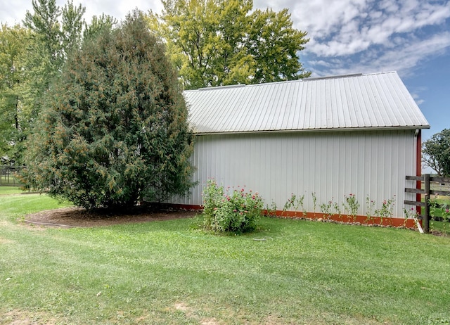 view of side of home featuring an outbuilding, fence, metal roof, and a yard