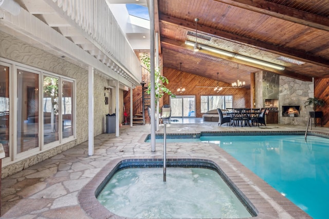 indoor pool with a fireplace, an indoor in ground hot tub, stairway, outdoor dining space, and a patio area