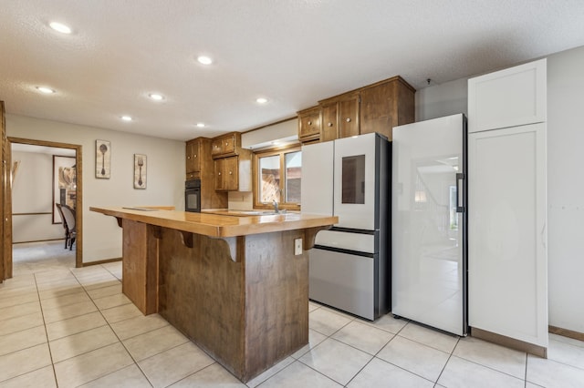 kitchen featuring oven, light tile patterned floors, a breakfast bar area, and freestanding refrigerator